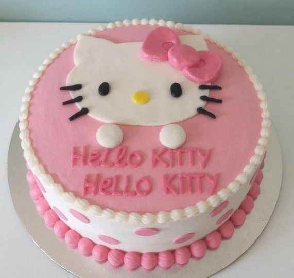 Round Hello Kitty cake with pink frosting, white polka dots, and a fondant Hello Kitty face featuring a pink bow and black whiskers